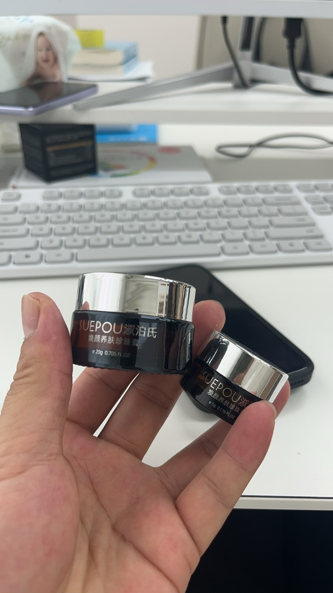 Source image for Hand Holding Two SUEPOU Cream Jars Over Office Desk