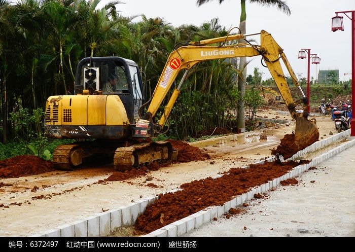 Source image for Yellow Excavator Digs Red Dirt Along Concrete Curb in Tropical Setting