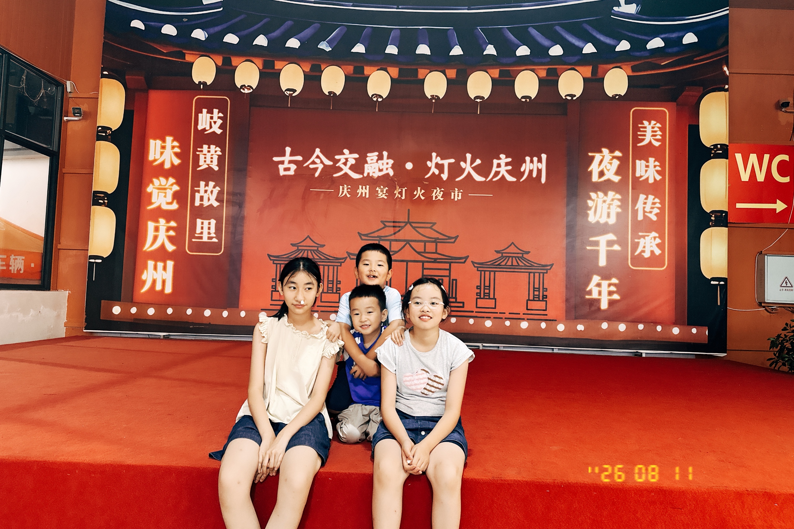 Source image for Four Kids Pose on Red Stage Before Glowing Chinese Lantern Backdrop